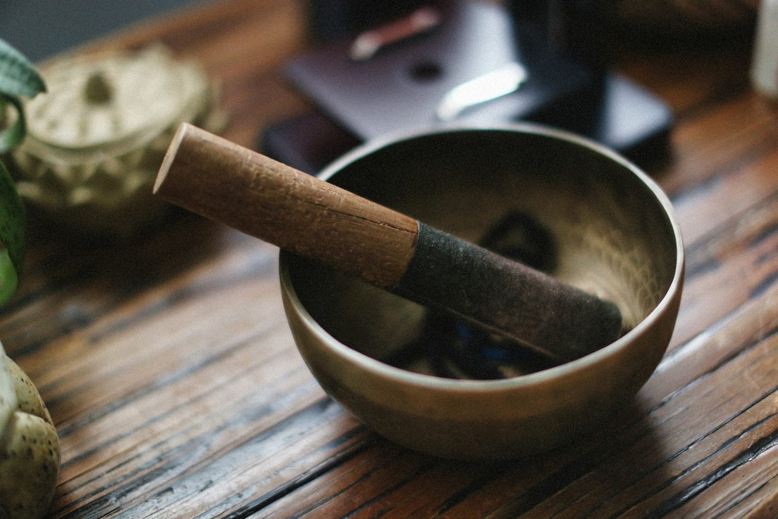 A bronze singing bowl and wooden striker resting on a wooden surface